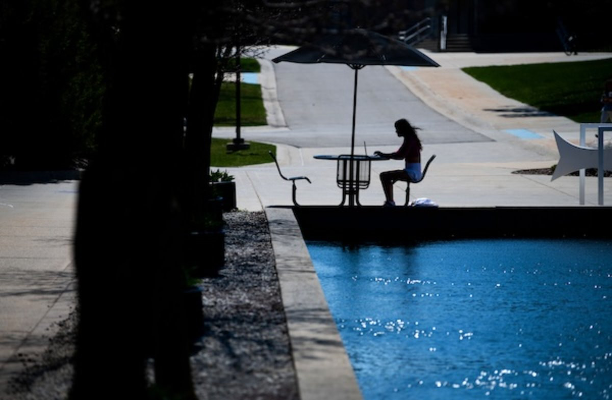 Student sitting at table under umbrella near Zumberge Pond on the GVSU Allendale campus