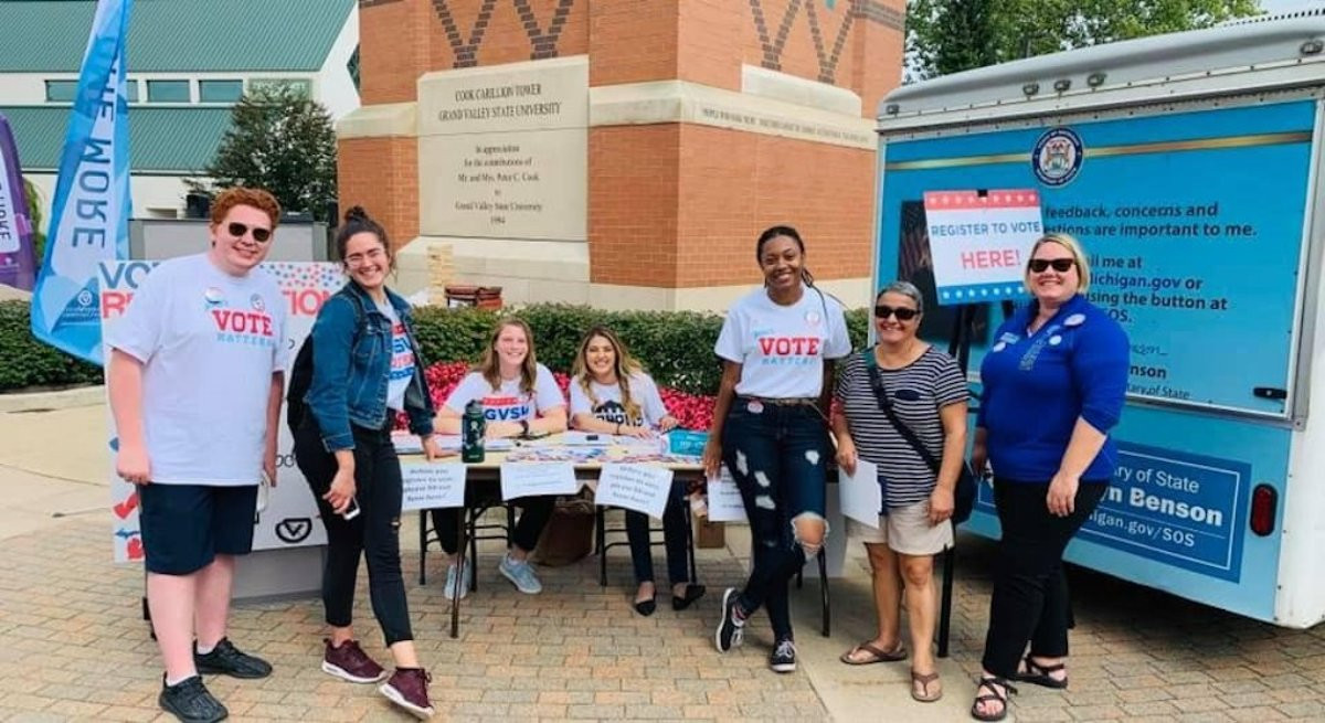group of people standing around a table promoting national voter day