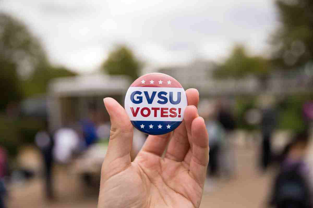 Hand holding up GVSU Votes! button with a blurry background