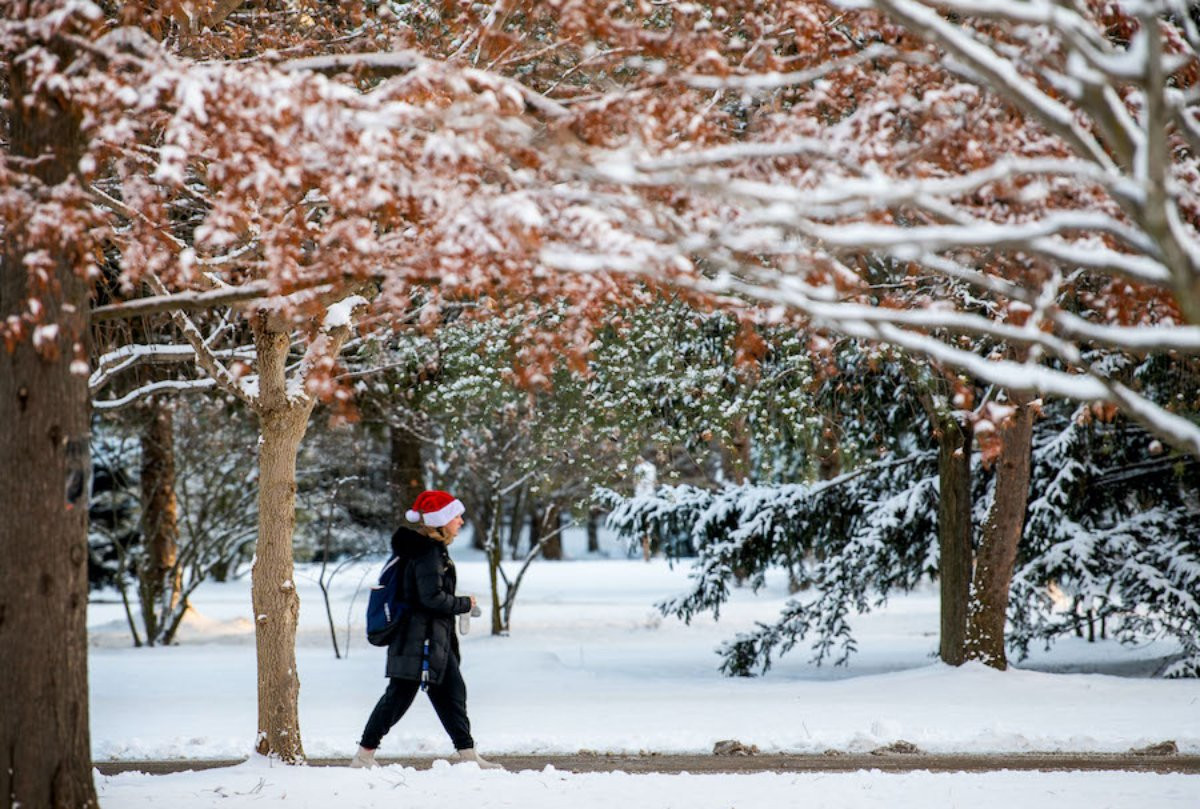 a student wearing a santa hat and walking on campus in the snow