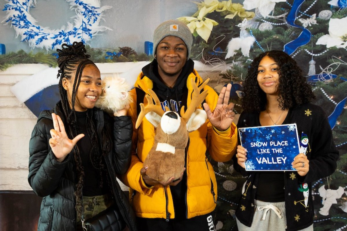 three people posing for the awkward photobooth holding a stuffed reindeer and a sign that reads Snow Place Like Grand Valley
