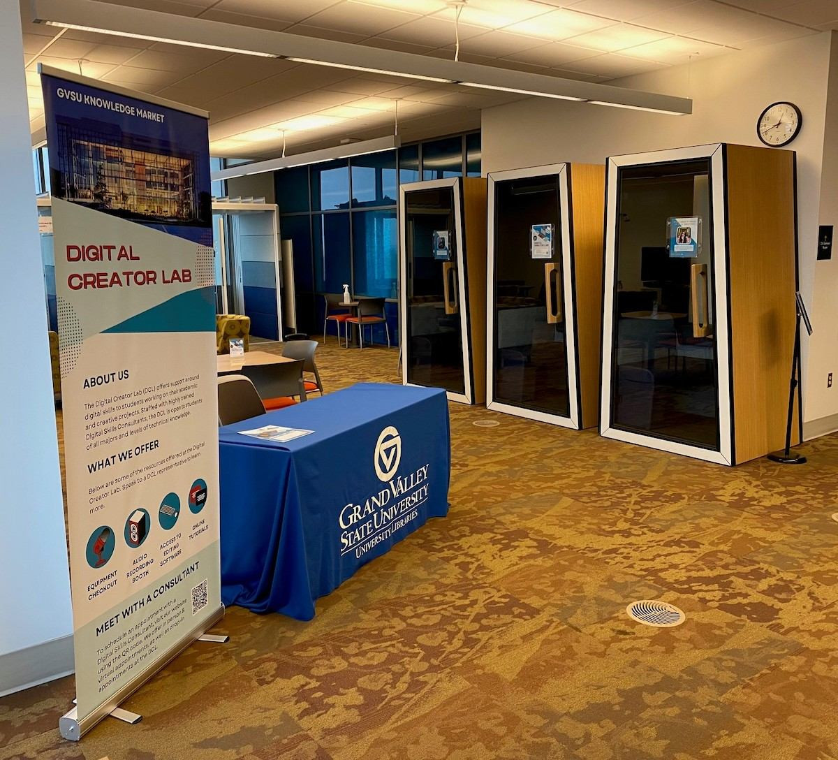 Signage that reads Digital Creator Lab set next to a table with a blue GVSU branded table cloth on it inside the Digital Creator Lab in the Mary Idema Pew Library.
