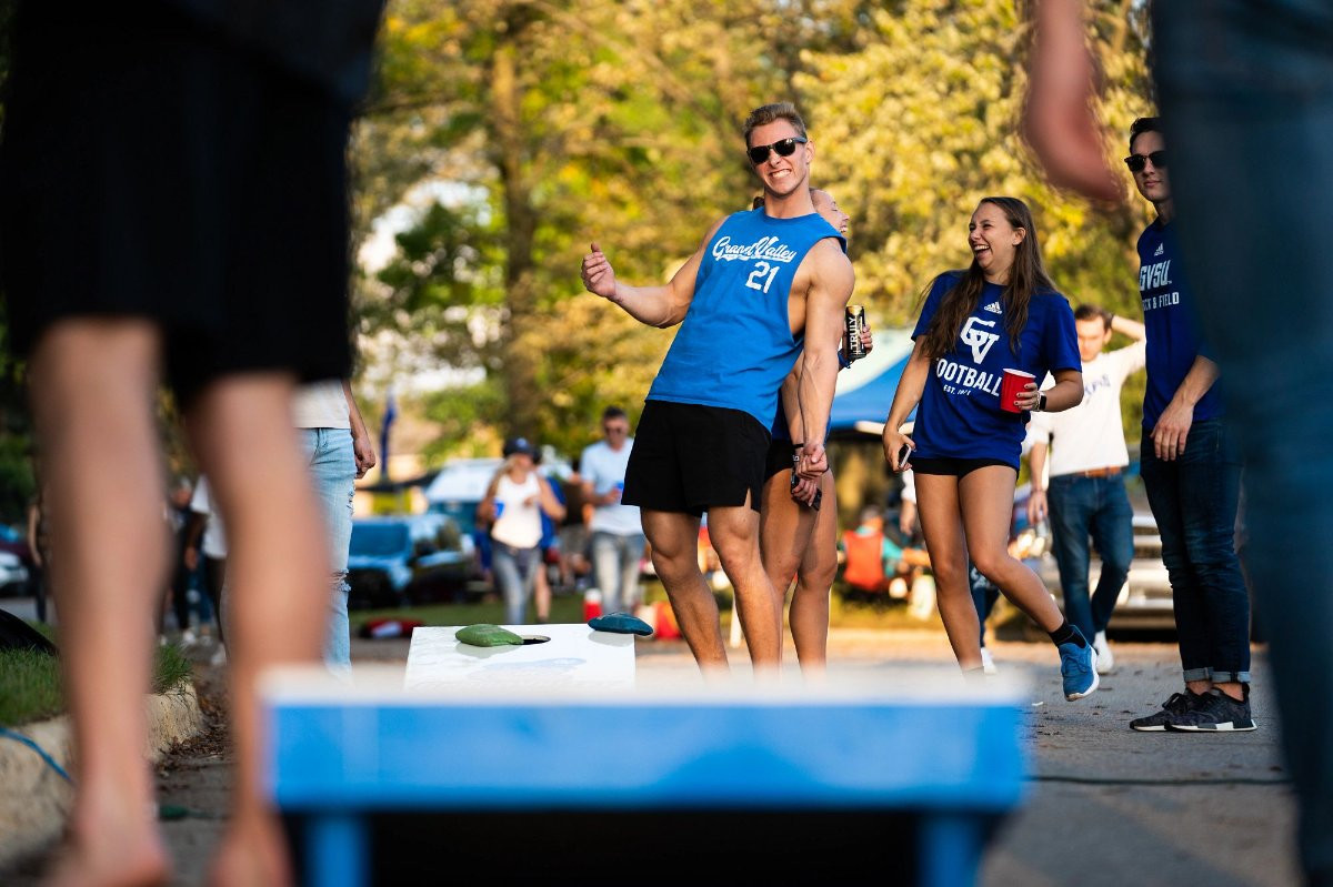 Student playing corn hole at a tailgate during the summer