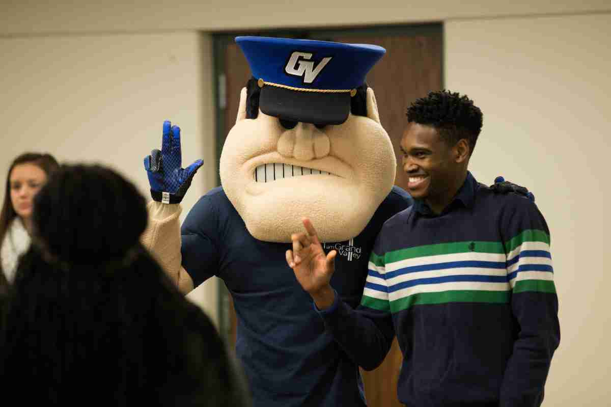 Louie the Laker holding up the anchor up symbol with a student