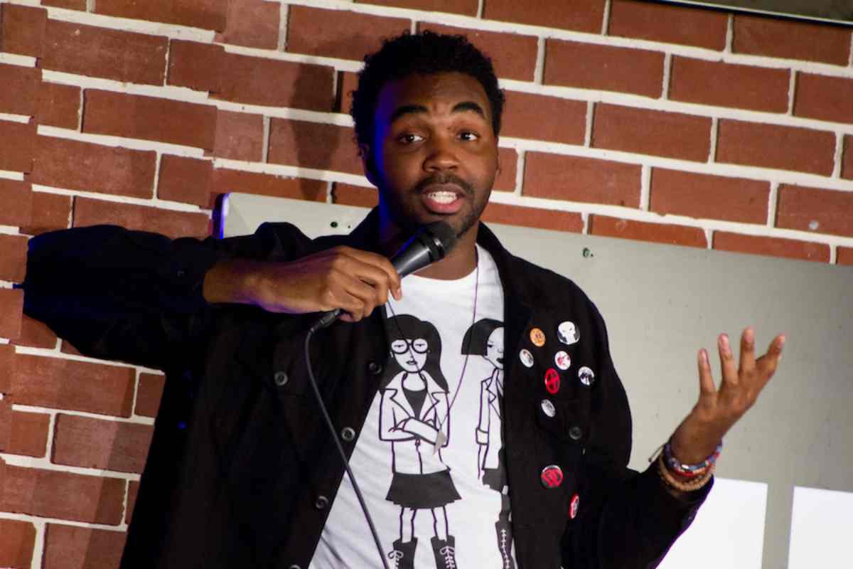 Comedian Lafayette Wright wearing a jean jacket and a shirt with people on it as he tells a joke