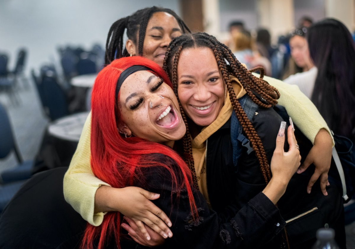 Three friends smiling and hugging each other at one of their organizations events