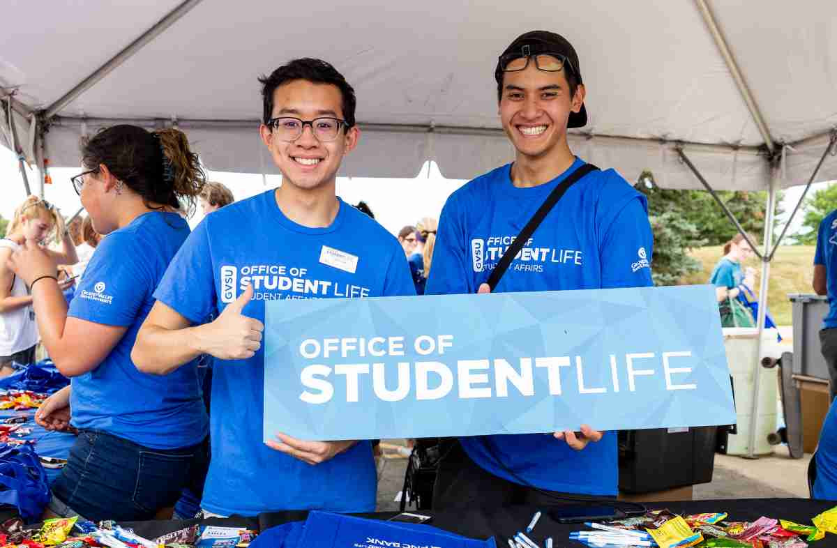 two student workers holding a office of student life sign