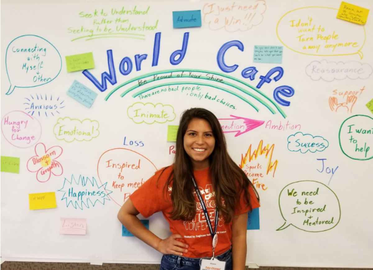 A student standing in front of a white board that says "World Cafe"