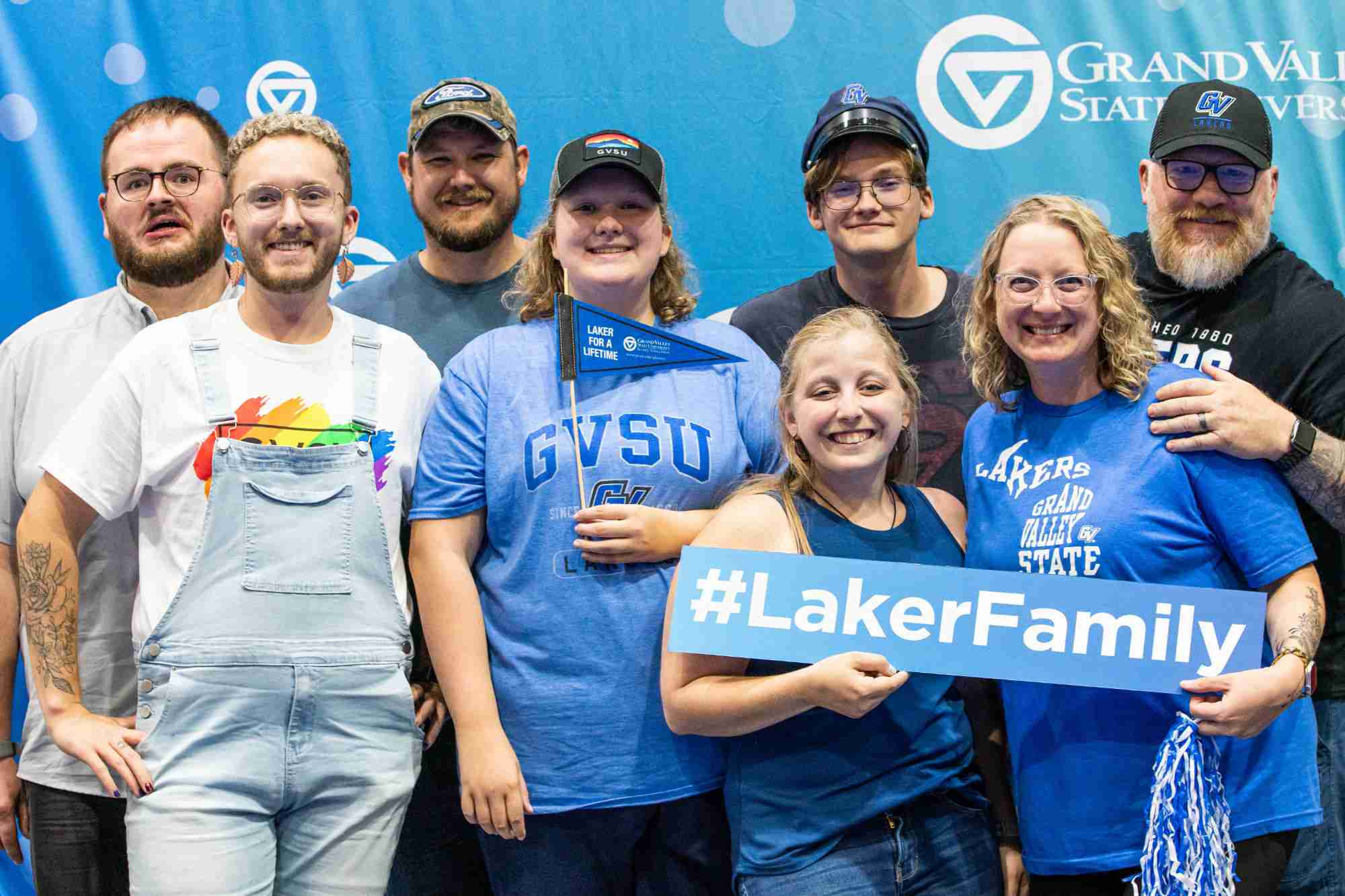 A family smiles for the camera holding a rectangular sign that reads "#LakerFamily"