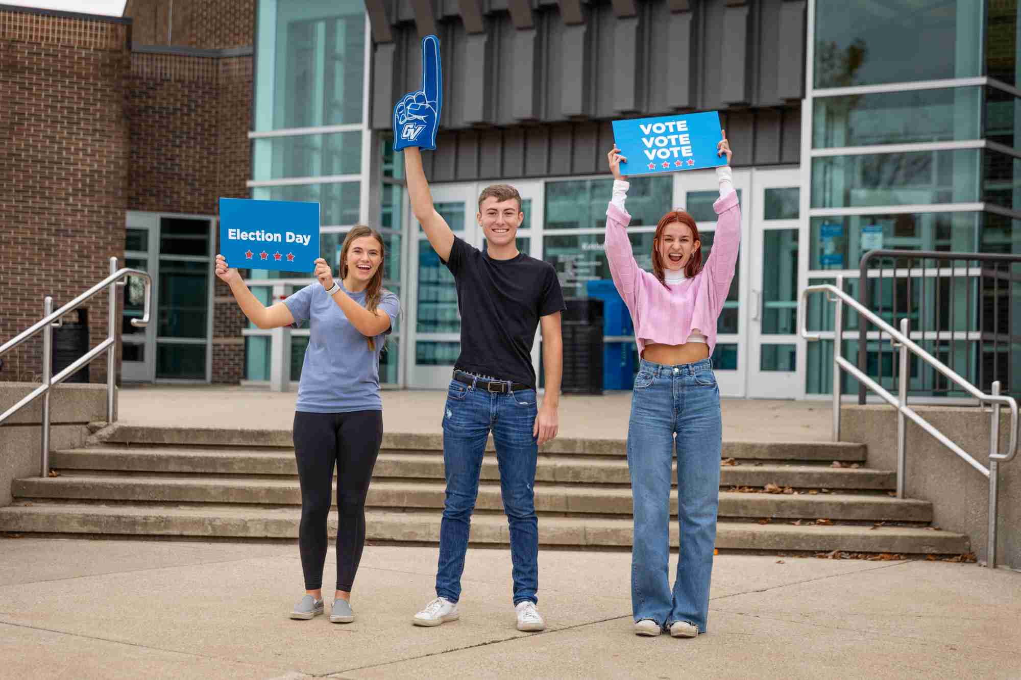 Three students standing in front of Kirkhof holding signs that read "election day" and "vote vote vote!"