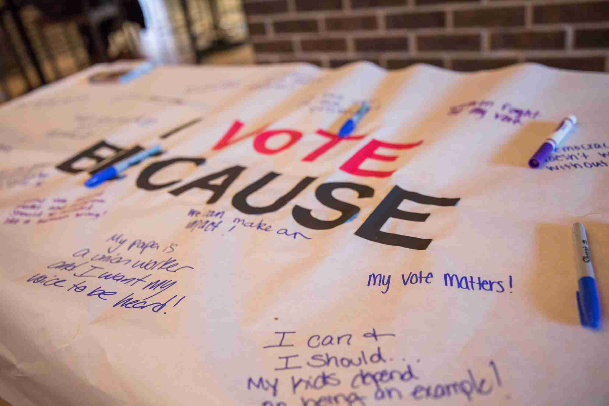 A white banner with text that reads "I vote because" with assorted handwritten messages