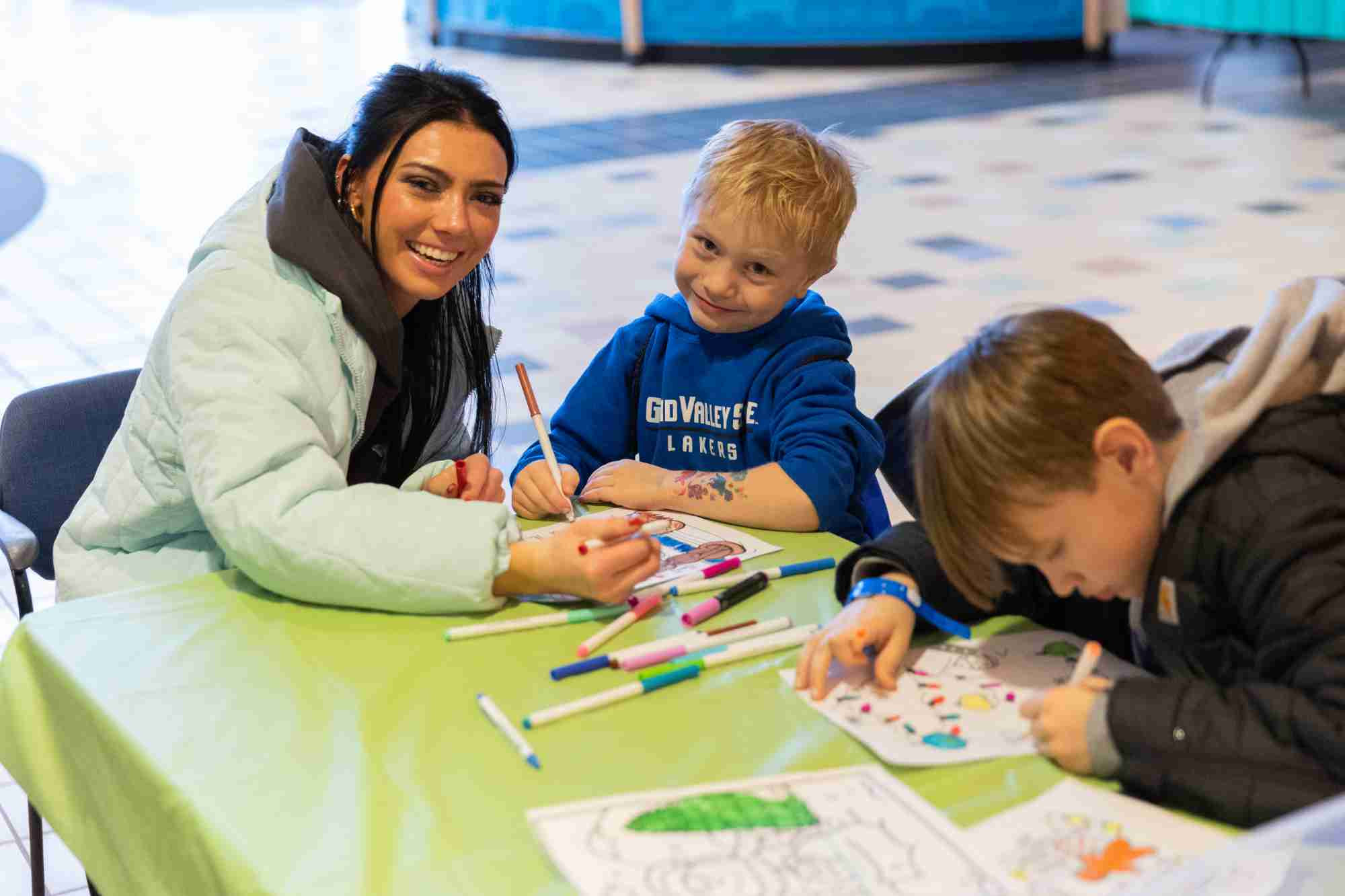 A girl who goes to GVSU smiling as she bonds with her younger sibling and colors a page