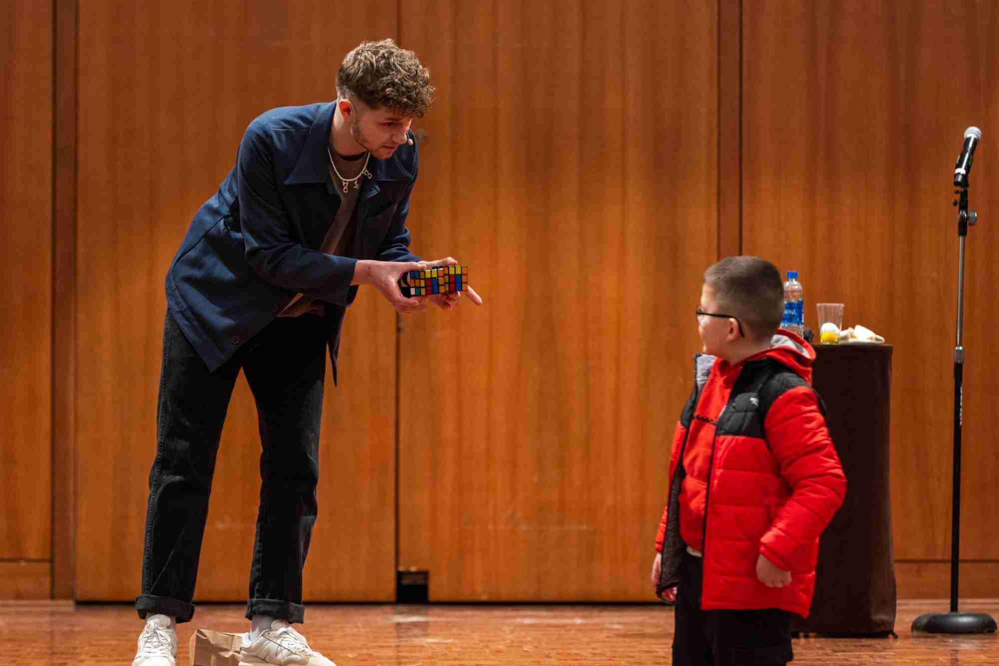 A performer holding a Rubiks Cube chats with a curious kid wearing a red coat