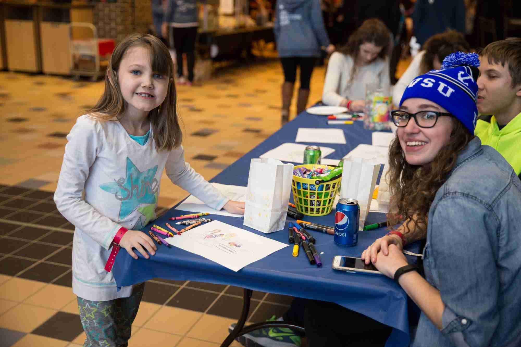 A GV student and a kid smile at the camera while coloring at a table