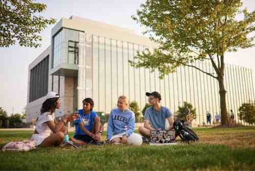 Four students spending spring break outside on the lawn in front of the library