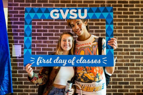 two students posing with a blue frame that says GVSU First Day of Classes