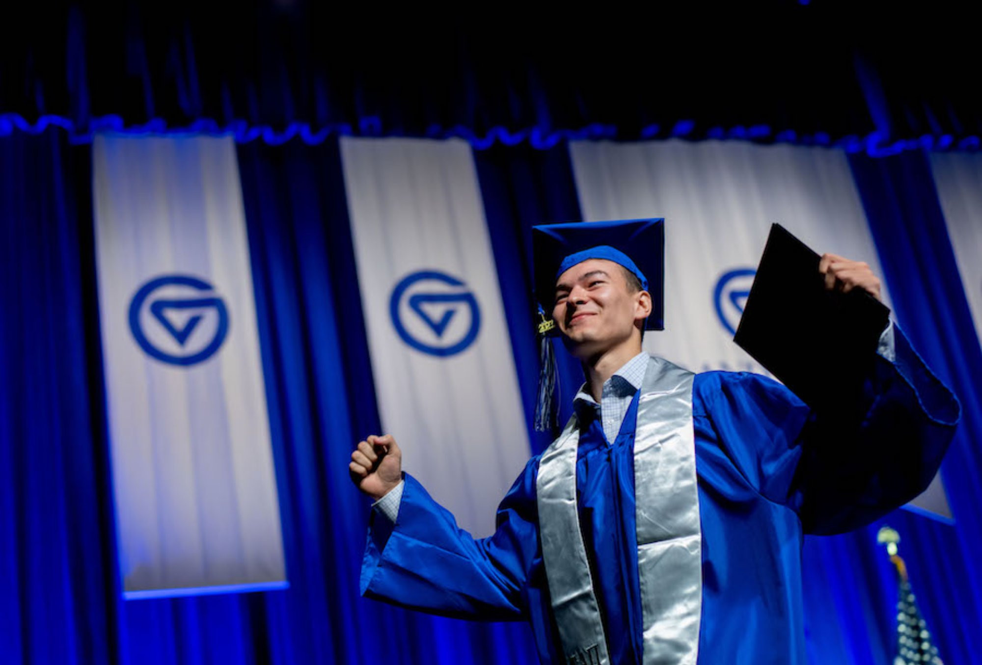 Student cheering and accepting his diploma on stage at graduation