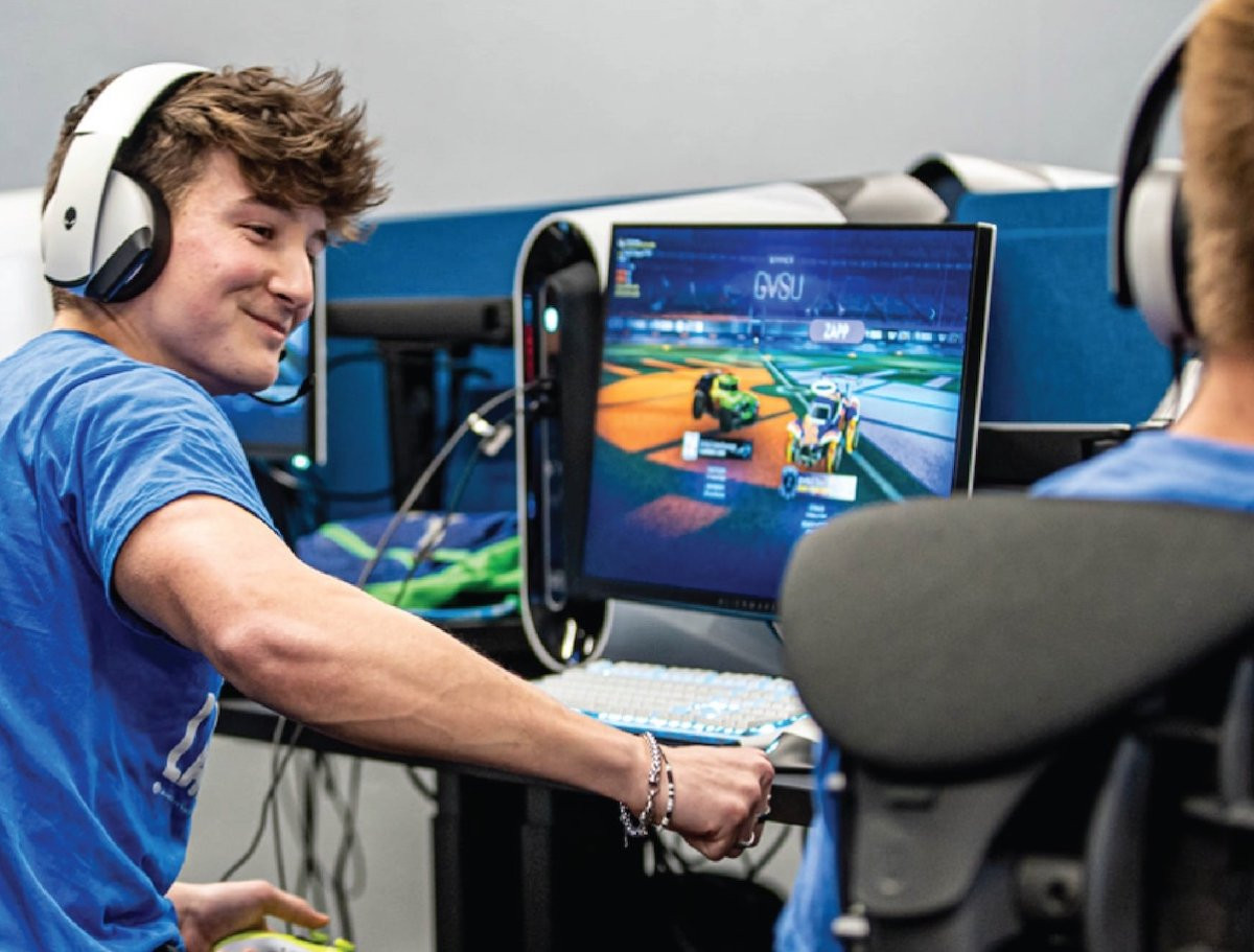 Two students wearing headphones and sitting at gaming stations in the GVSU Esports center.