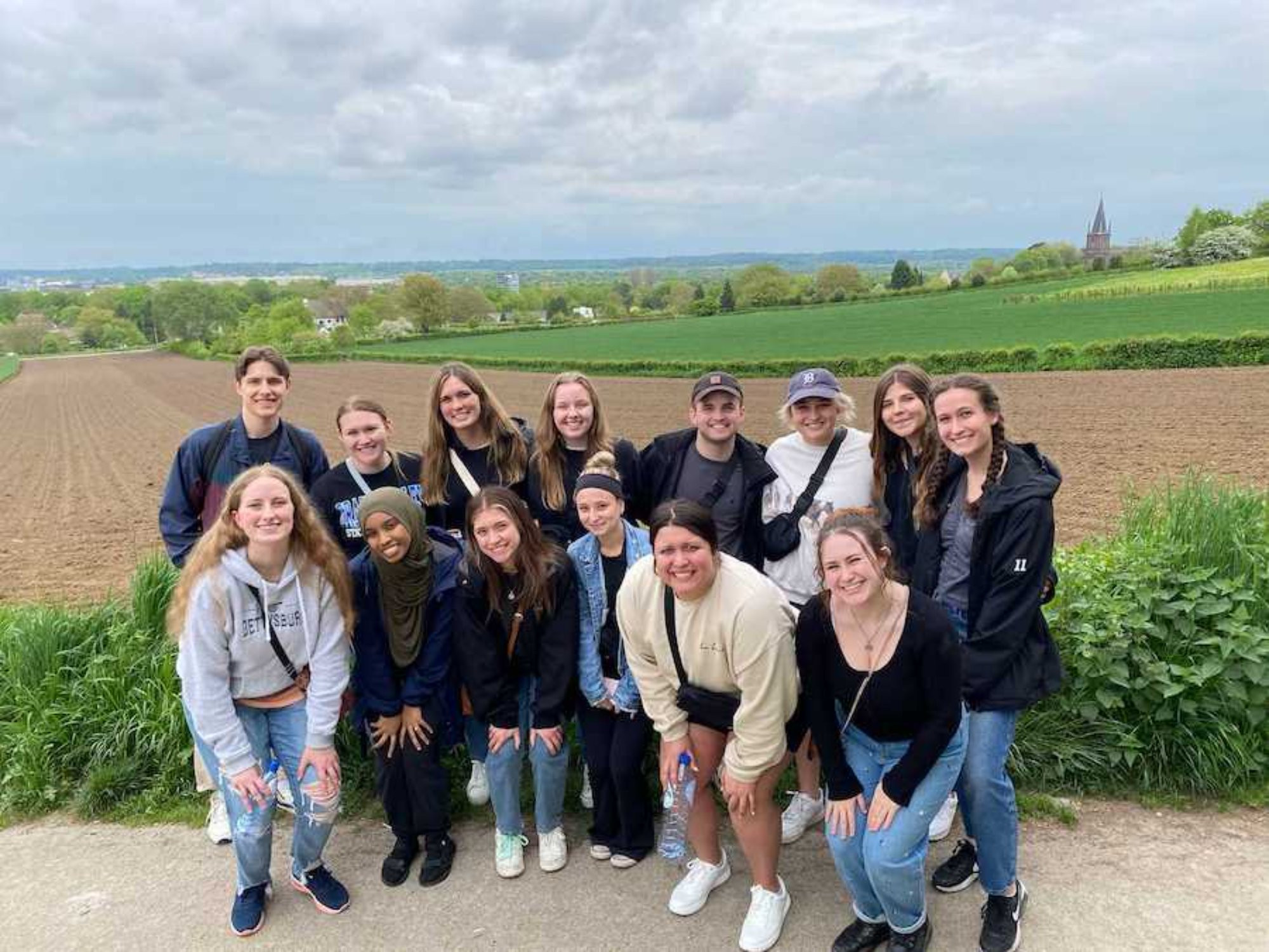 group of students studying abroad and taking a picture in front of a pretty farming landscape
