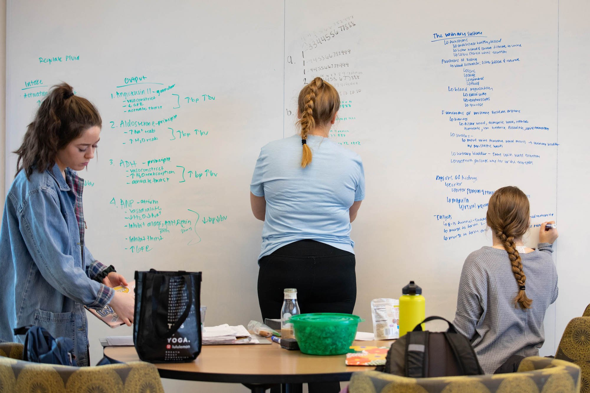 three students writing on the whiteboards in the library to study