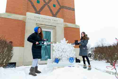 Students carving a snowflake out of ice in front of the clocktower