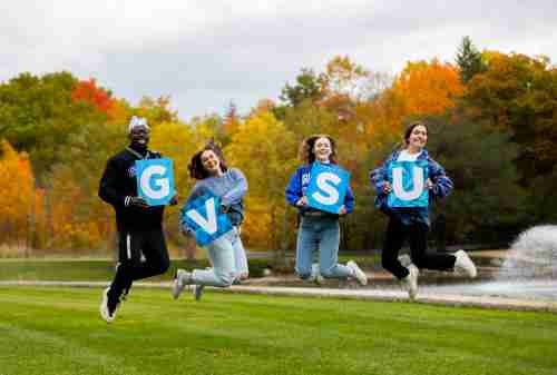 students jumping with individual letters that spell GVSU