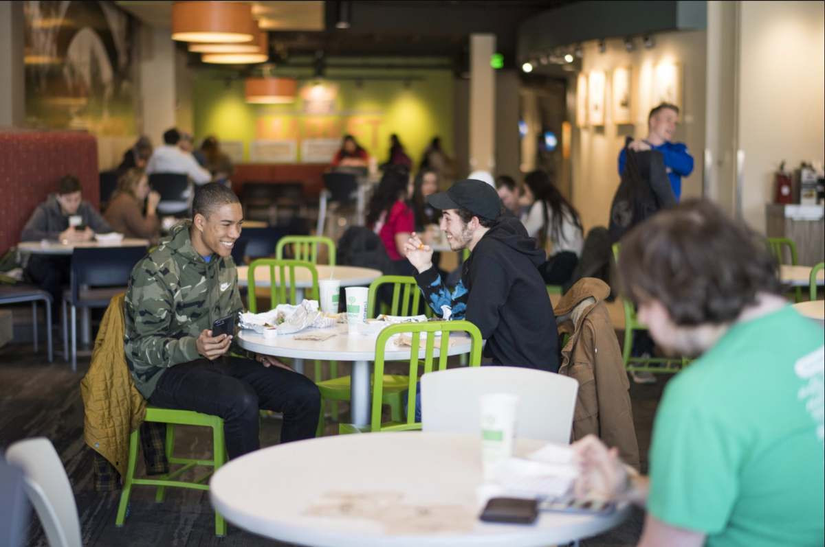 Two students sitting in the dining hall eating and laughing