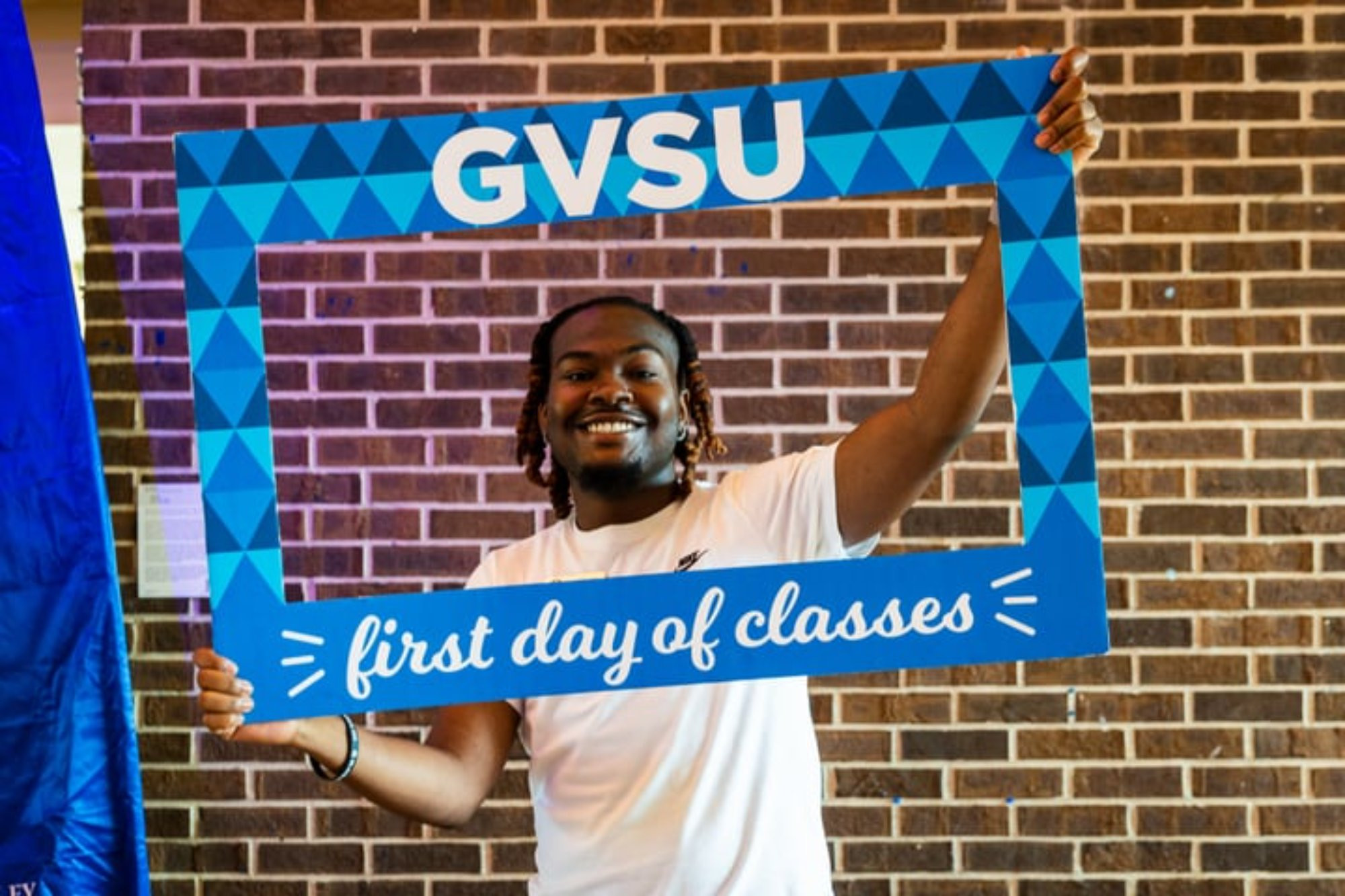 A student smiling and holding a blue frame that reads GVSU First Day of classes!