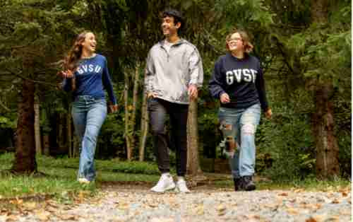 Three students in GV apparel walking on trail with leaves on the ground