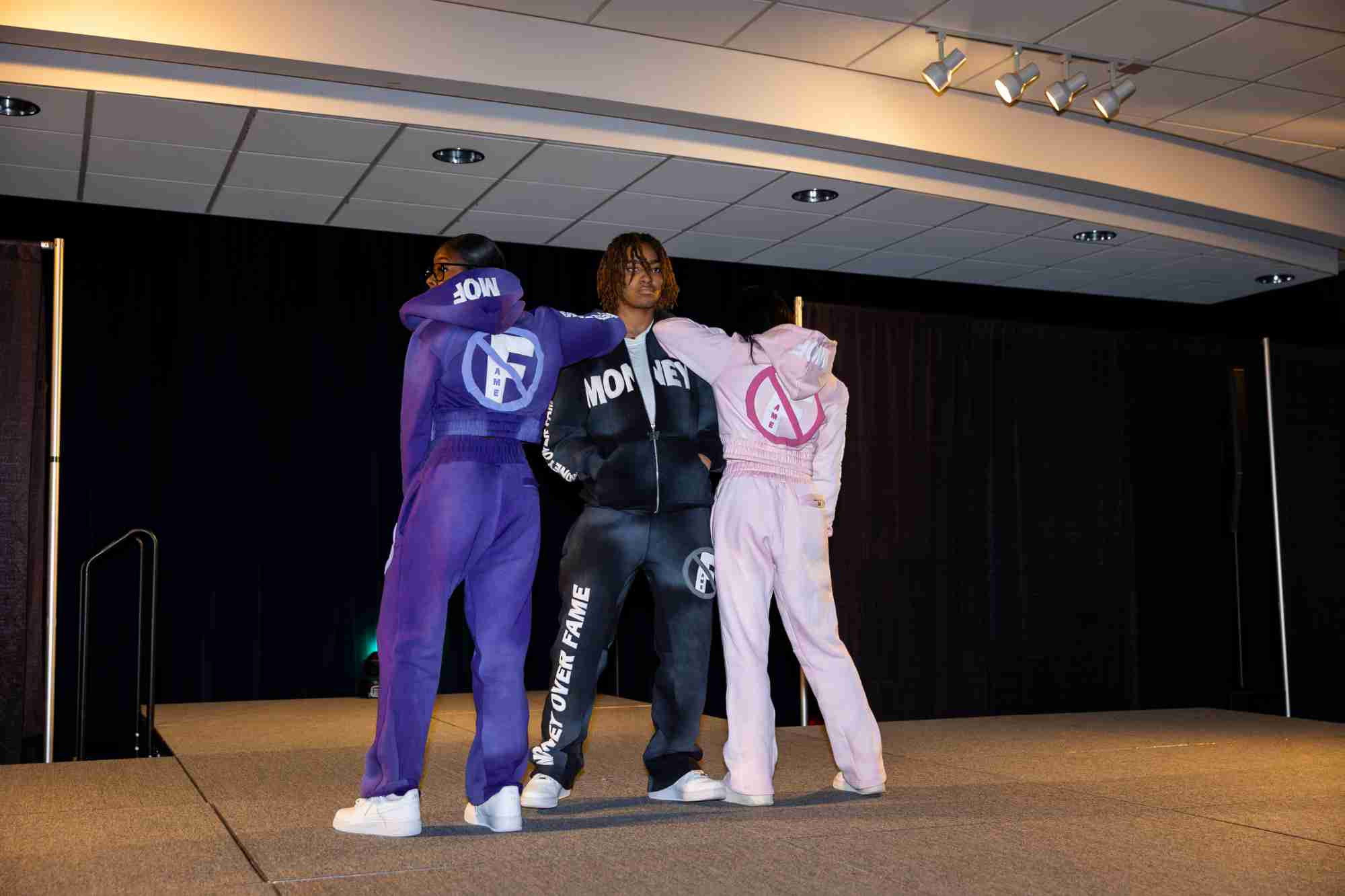 Three Model Entertainment students dressed in different colored sweat suits posing onstage