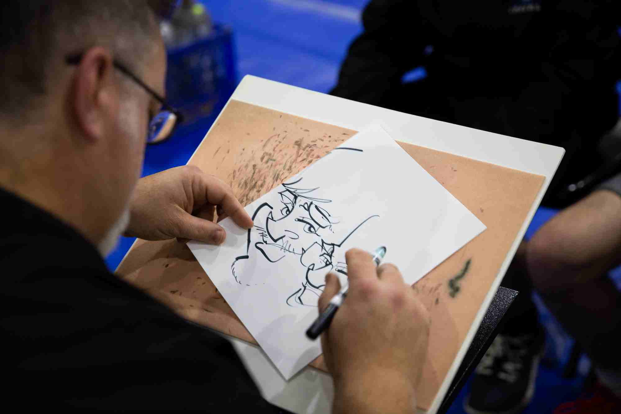 An artist drawing a cartoon portrait of students