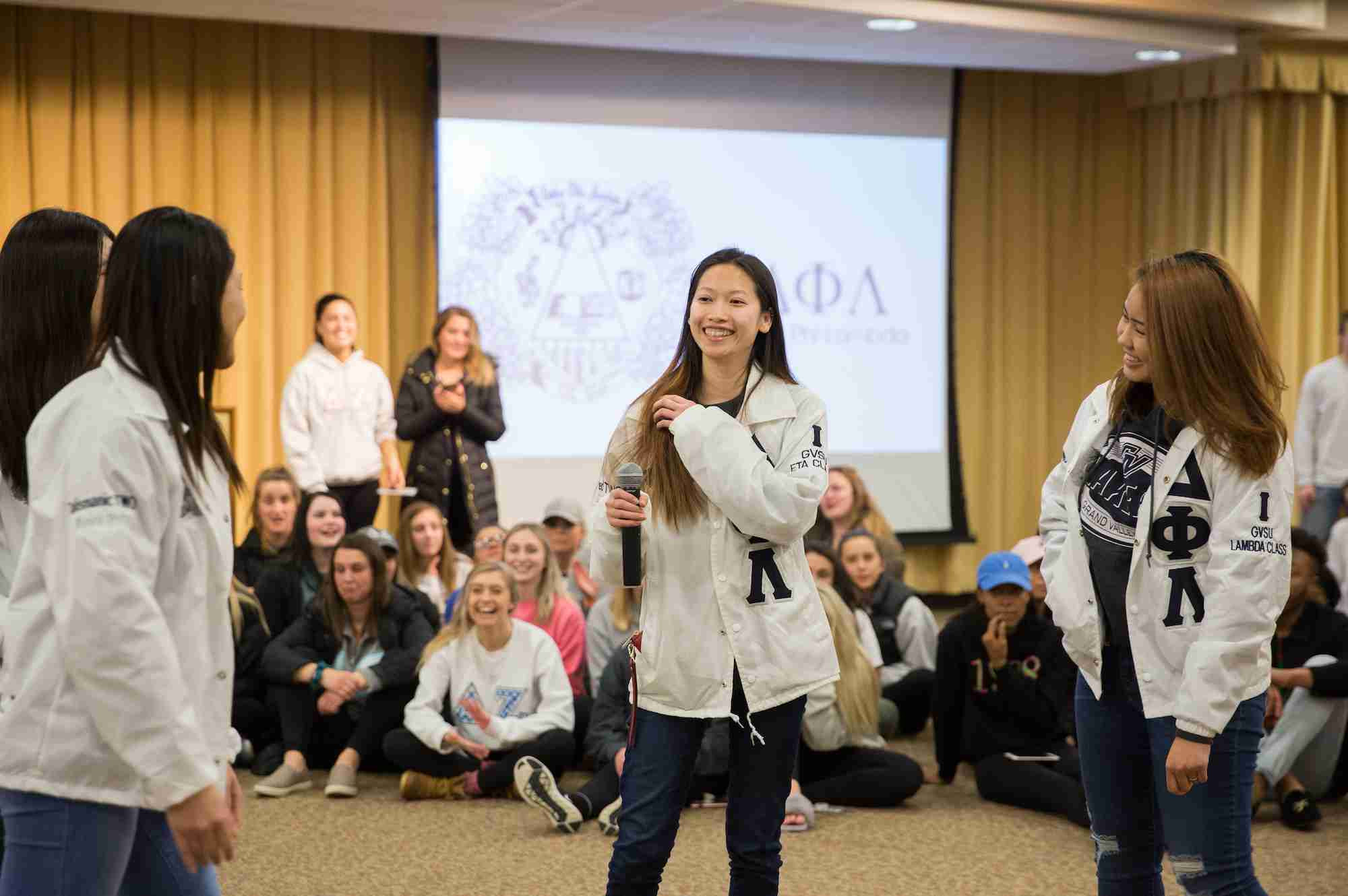 three greek life members standing in the middle of the room with a microphone