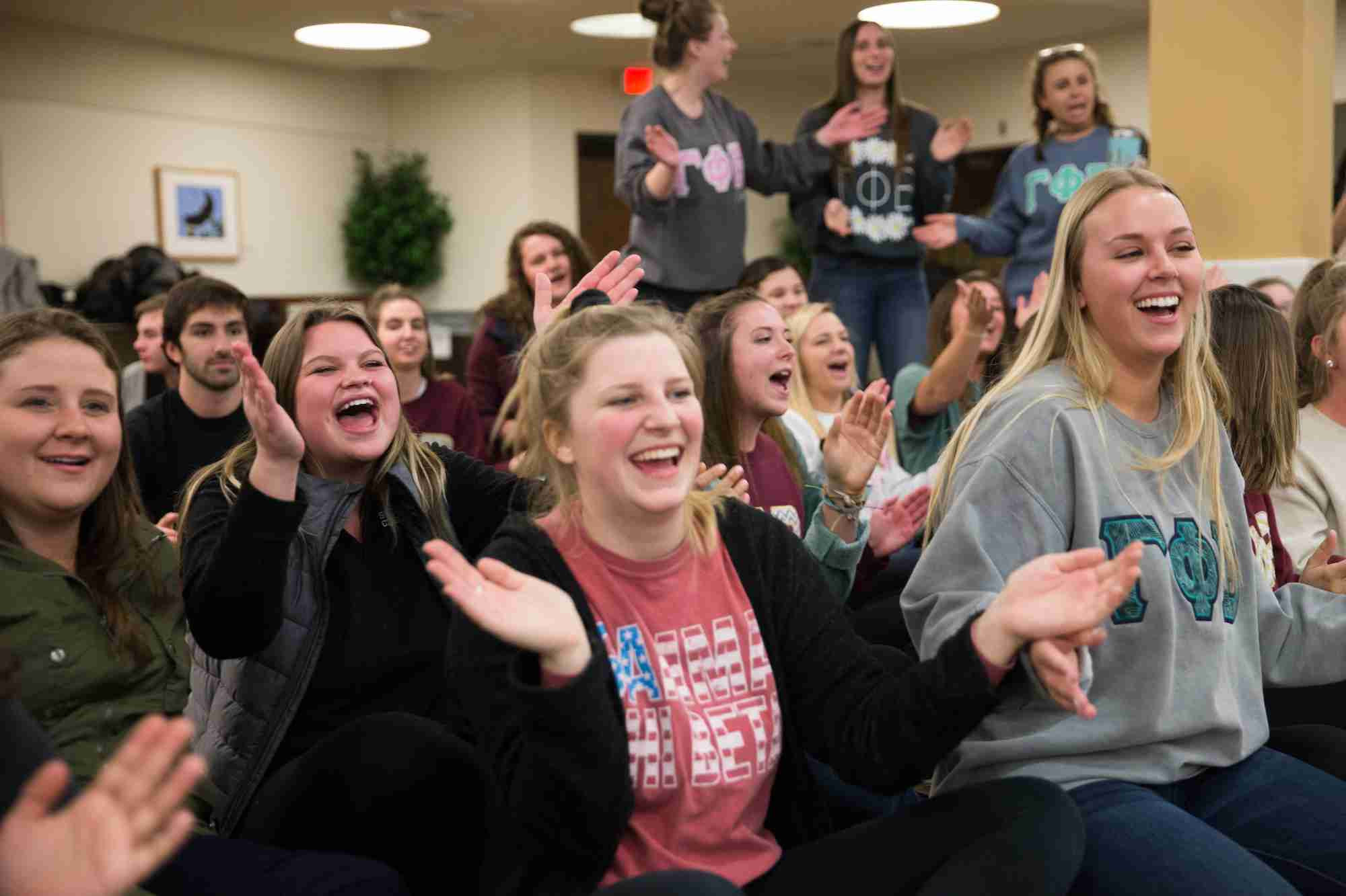 a crowd of greek life laughing and clapping