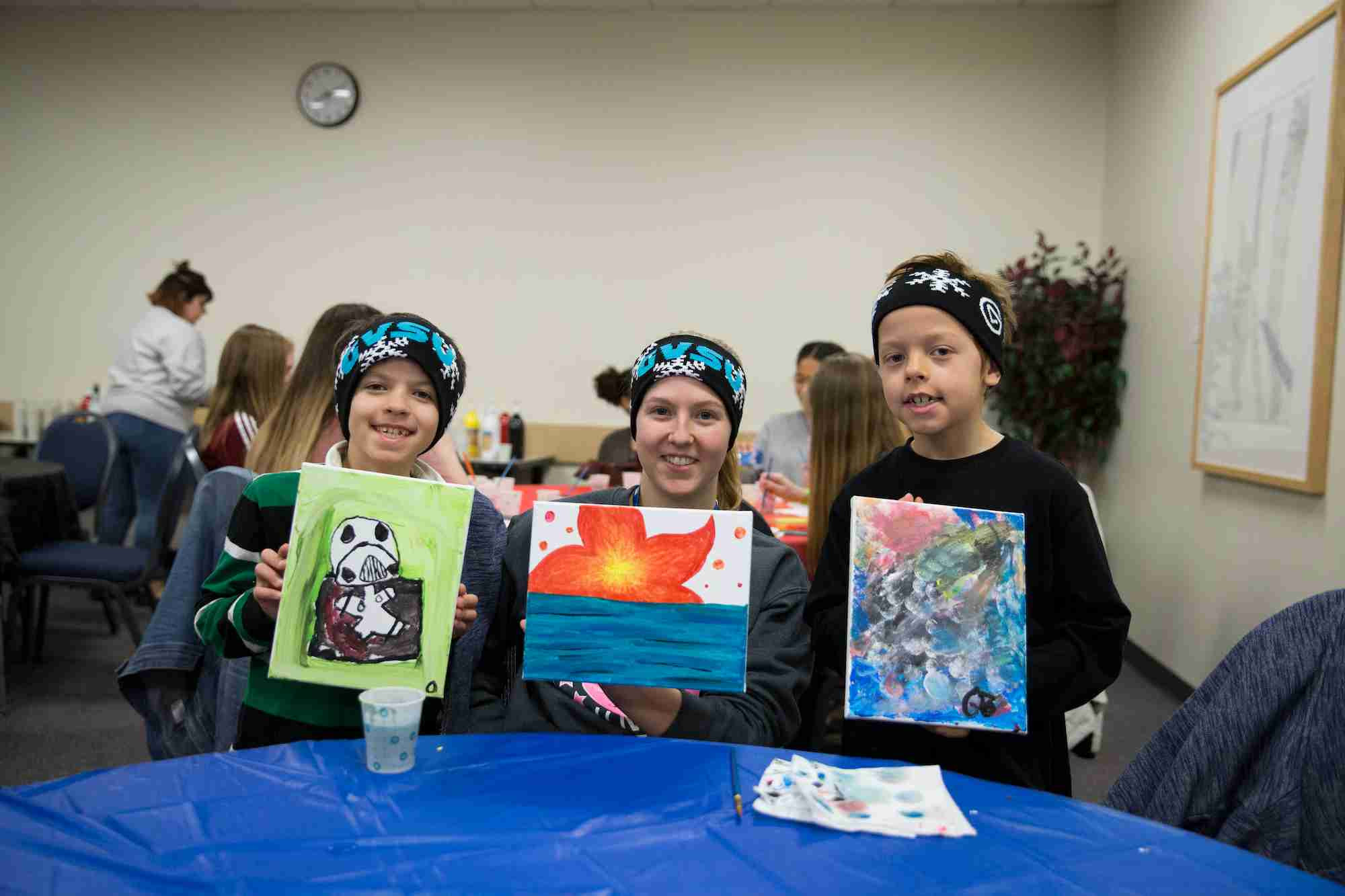 Student and siblings holding up their paintings