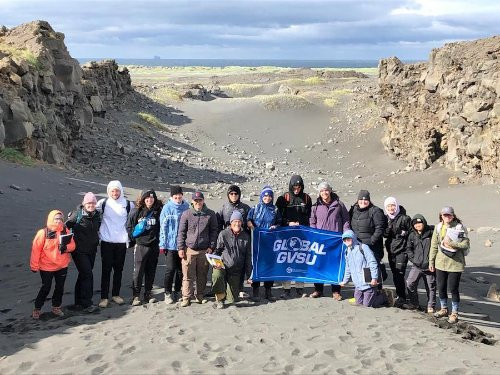 a group of students holding up a flag that reads Global GVSU in front of a crater