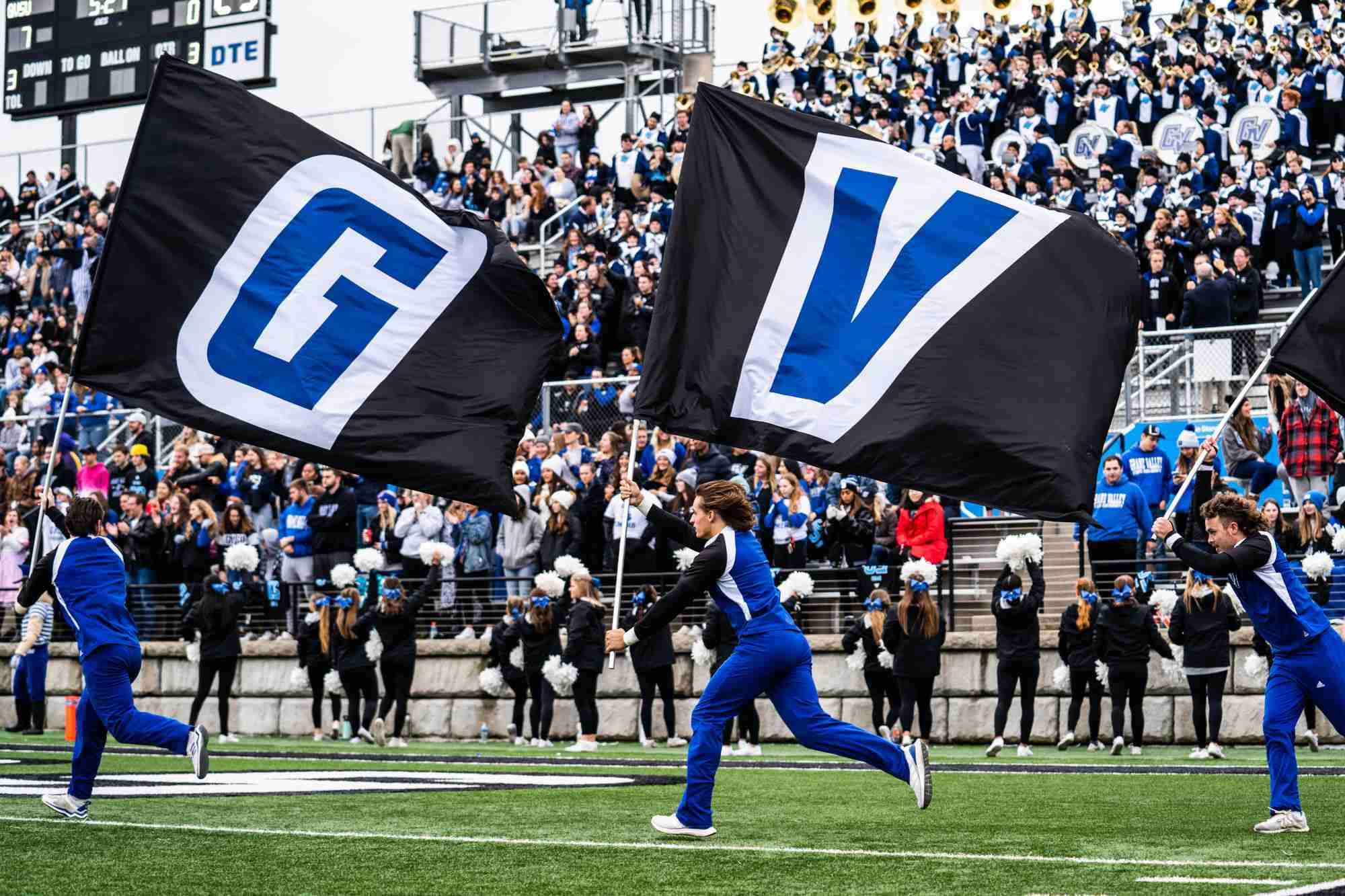 Cheerleaders running GV flag across the football field 