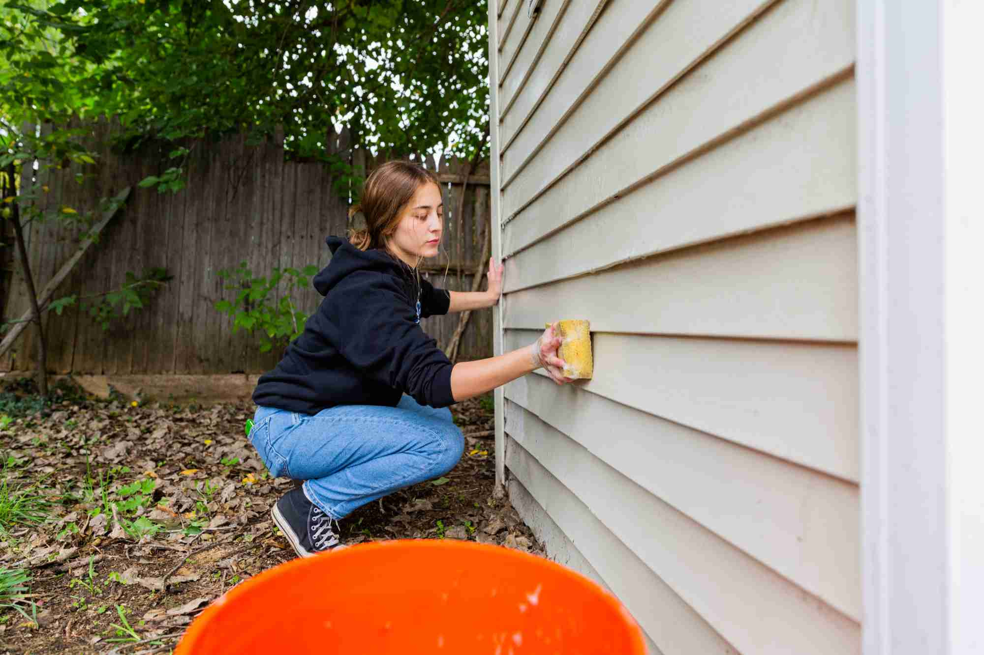 Student cleaning the siding on a house with a sponge