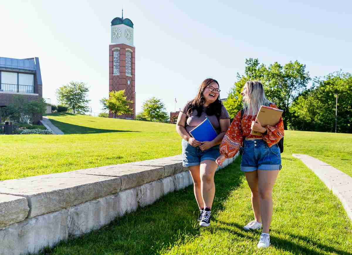 Two students walking through campus with book sin their arms.