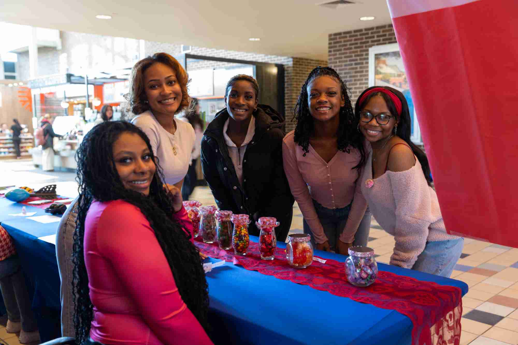 Five students gathered around a table covered in Valentine's Day decorations, smiling and posing for the camera