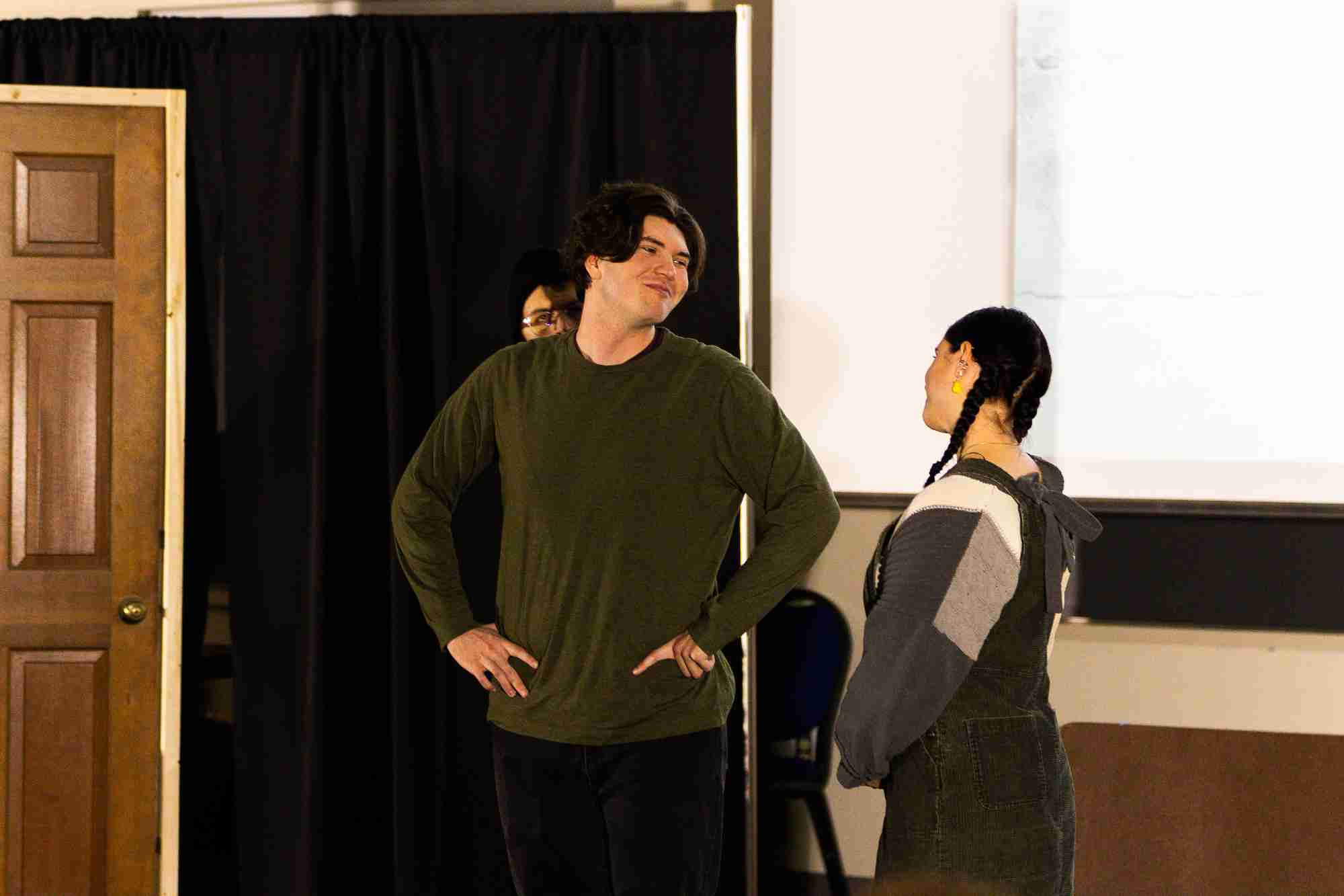 Two students smile and look at each other while standing next to a prop door