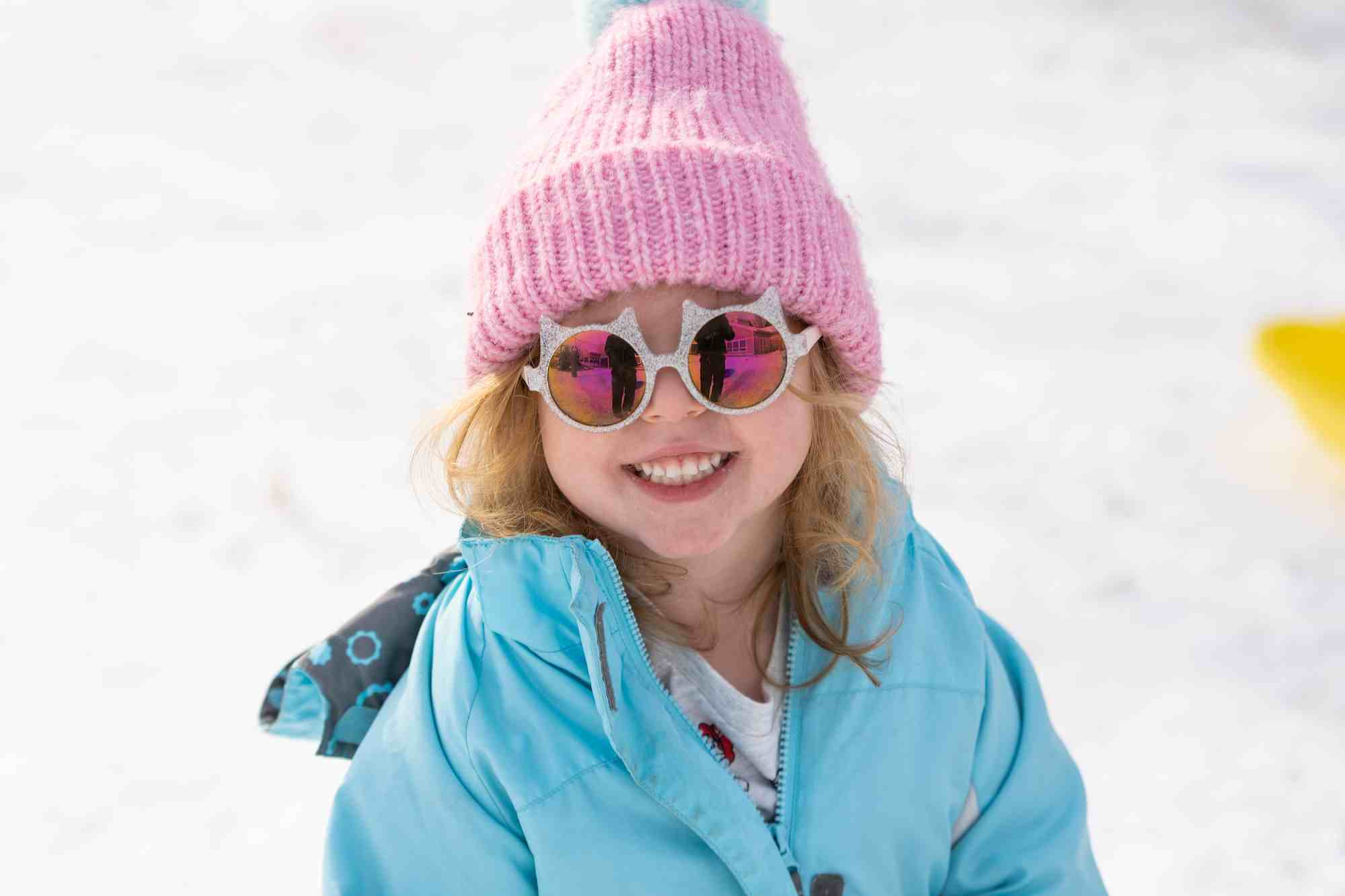 A kid in their hat and sun glasses smiling at the camera