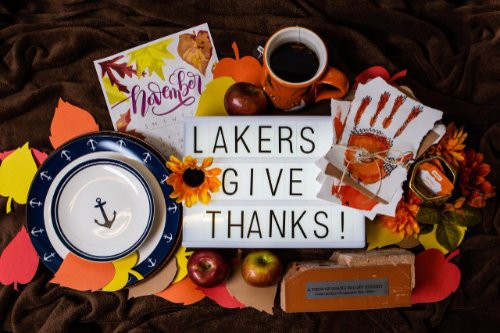 A plate with anchors on it, a calendar for the month of November, a mug of tea, some drawings of turkeys, decorative orange flowers, a brick from the clock tower, and a sign that reads "Lakers give thanks!"