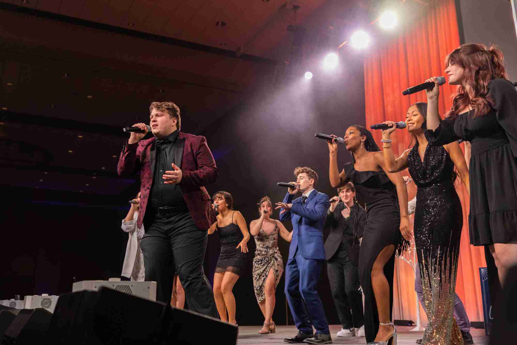 A group of formally dressed students singing into microphones onstage at Presidents' Ball